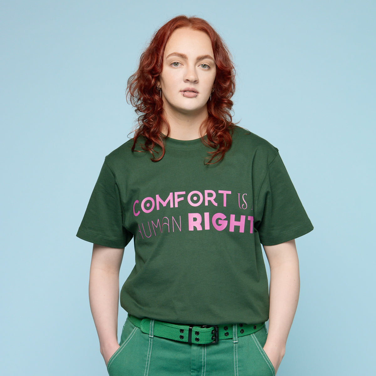 Person wearing a green Pride t-shirt with &#39;COMFORT IS RIGHT&#39; text on a light blue background