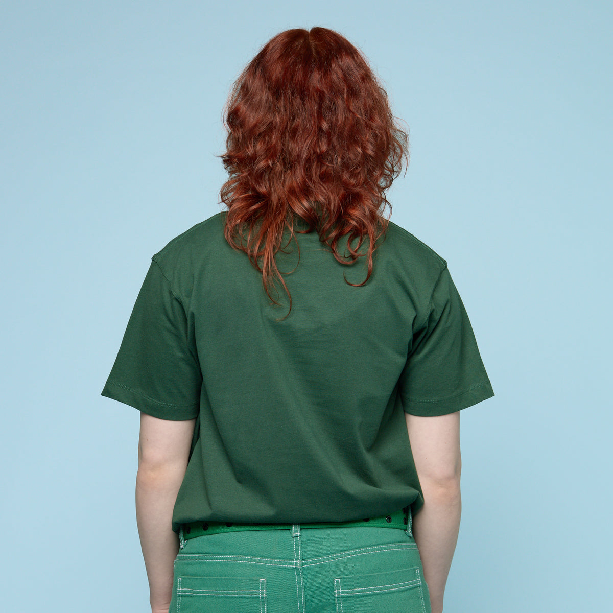 Person wearing a green t-shirt and pants against a light blue background