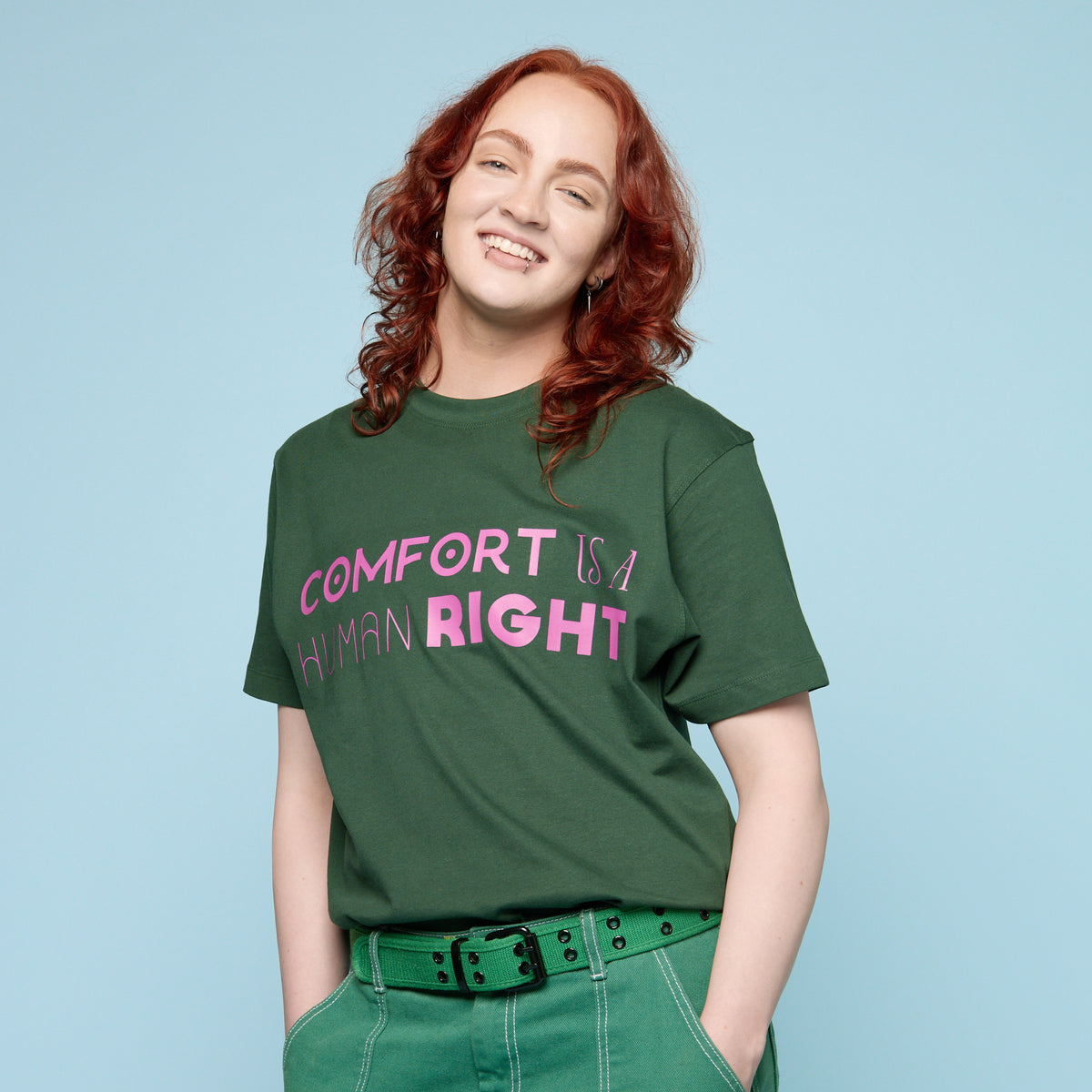 Person wearing a green Pride t-shirt with &#39;Comfort is a Human Right&#39; text on a light blue background