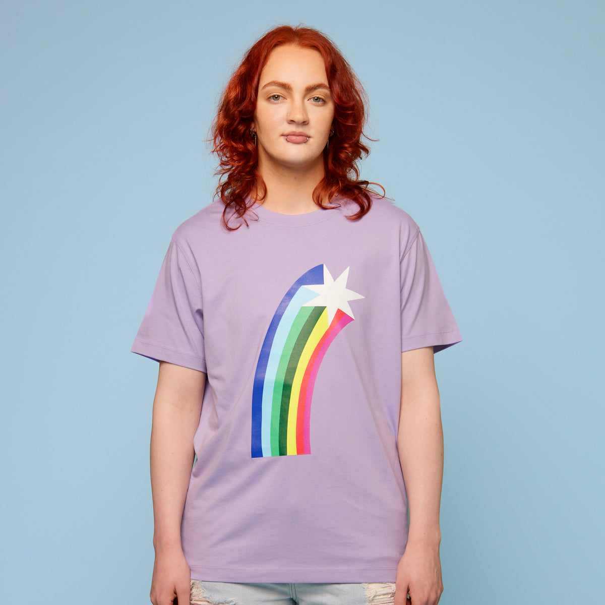 Person wearing a purple pride t-shirt with a rainbow and star design on a light blue background