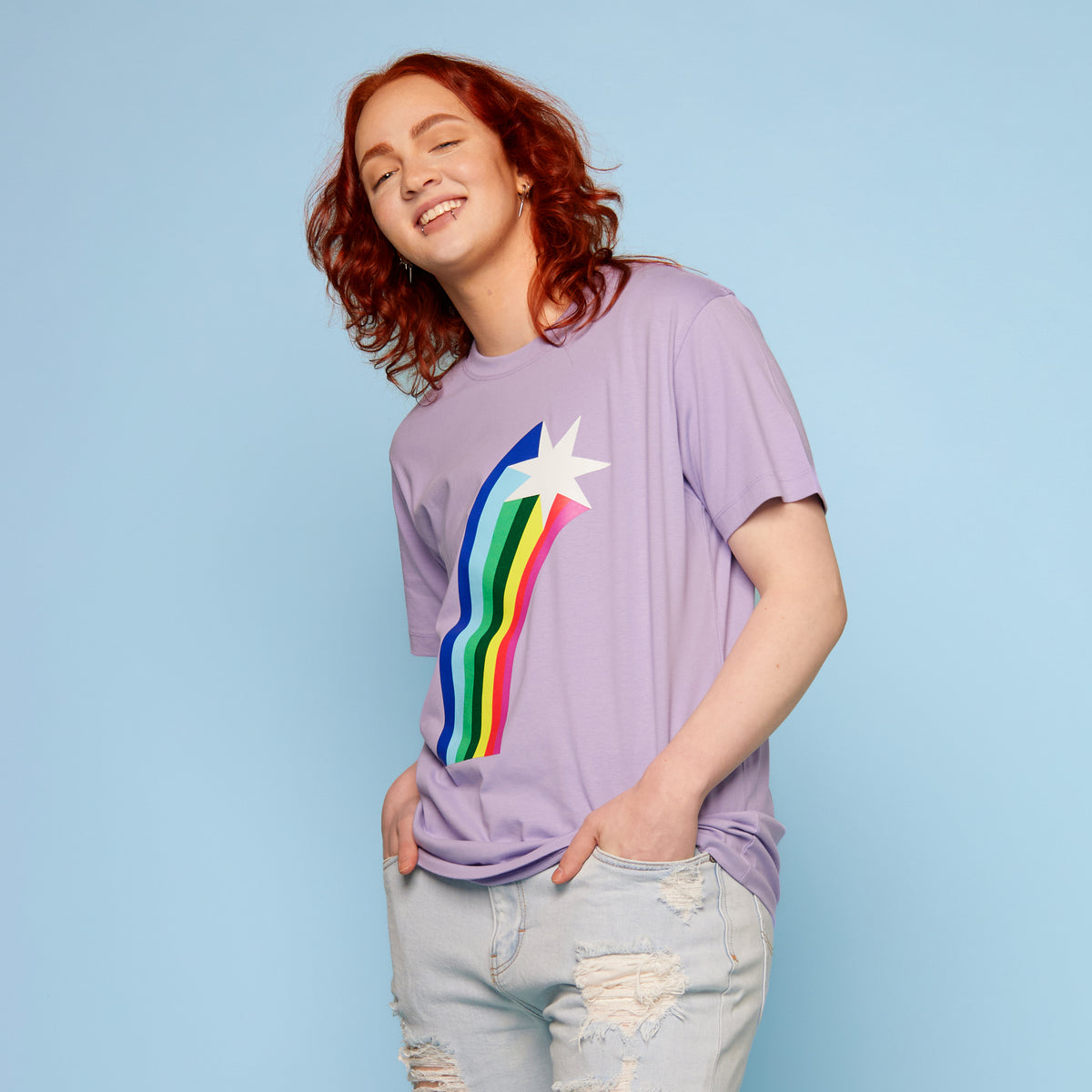 Person wearing a purple pride t-shirt with a rainbow and star design on a light blue background