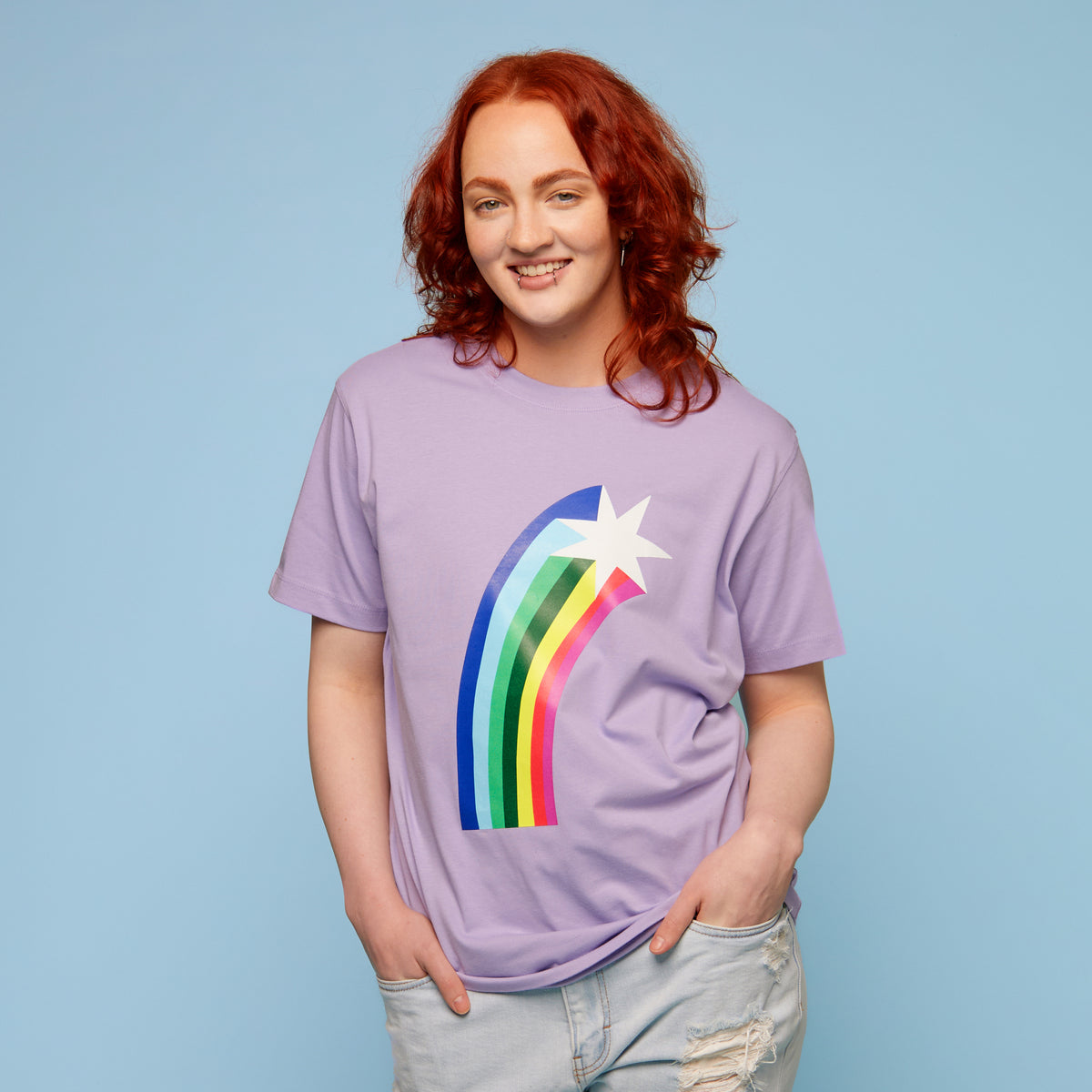 Person wearing a purple pride t-shirt with a rainbow and star design on a light blue background